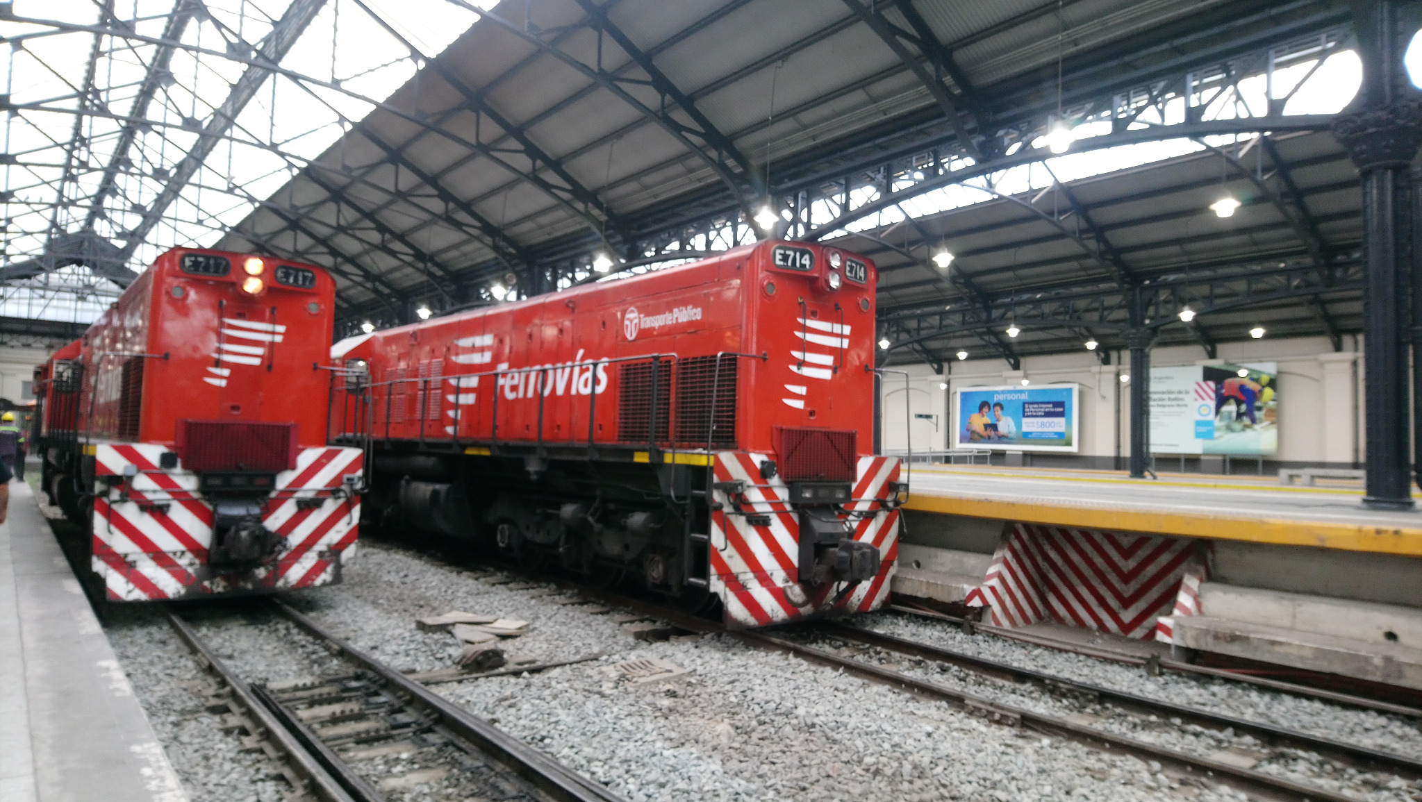 Dos locomotoras rojas de Ferrovías bajo el techo de una estación